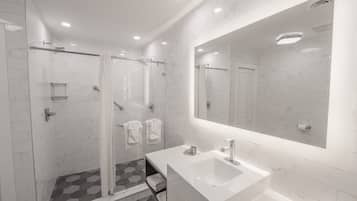 A modern bathroom with a glass shower enclosure, a large mirror, and a white sink.