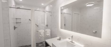 A modern bathroom with a glass shower enclosure, a large mirror, and a white sink.