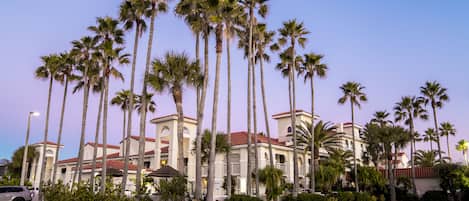 A hotel with a symmetrical facade, palm trees, and a well-maintained lawn.