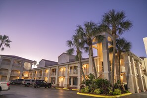 A hotel with multiple balconies, palm trees, and a parking lot with several cars.