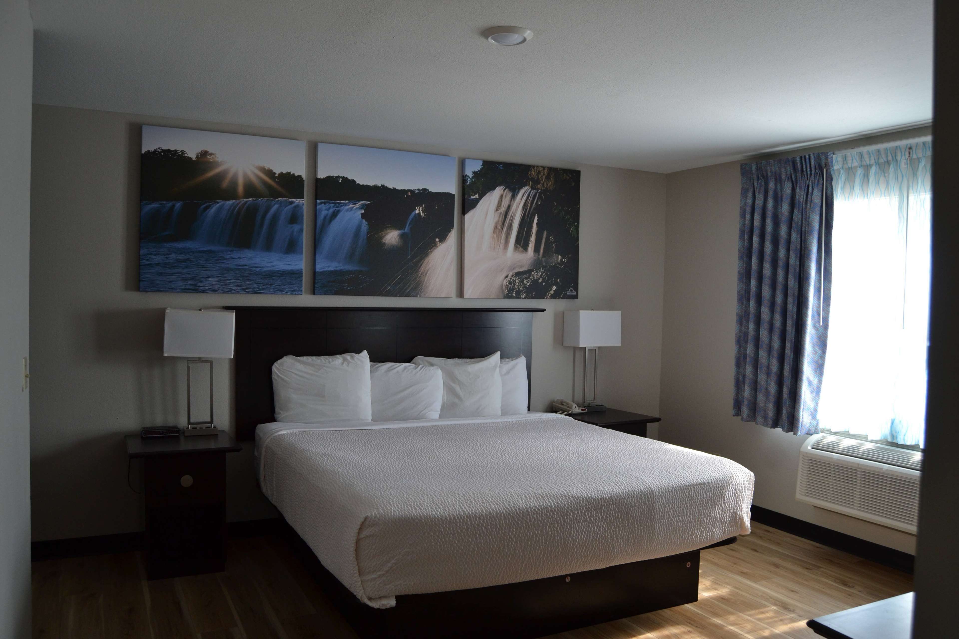 A hotel room with a large bed, two bedside tables, a wall-mounted TV, and a window with curtains.