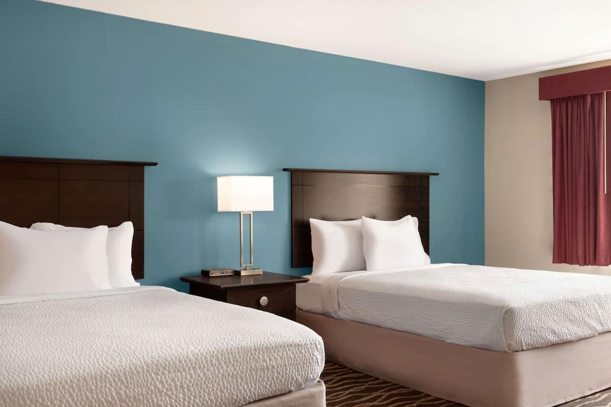 Habitación de hotel con dos camas, una mesita de noche, una lámpara y un ventanal con cortinas.