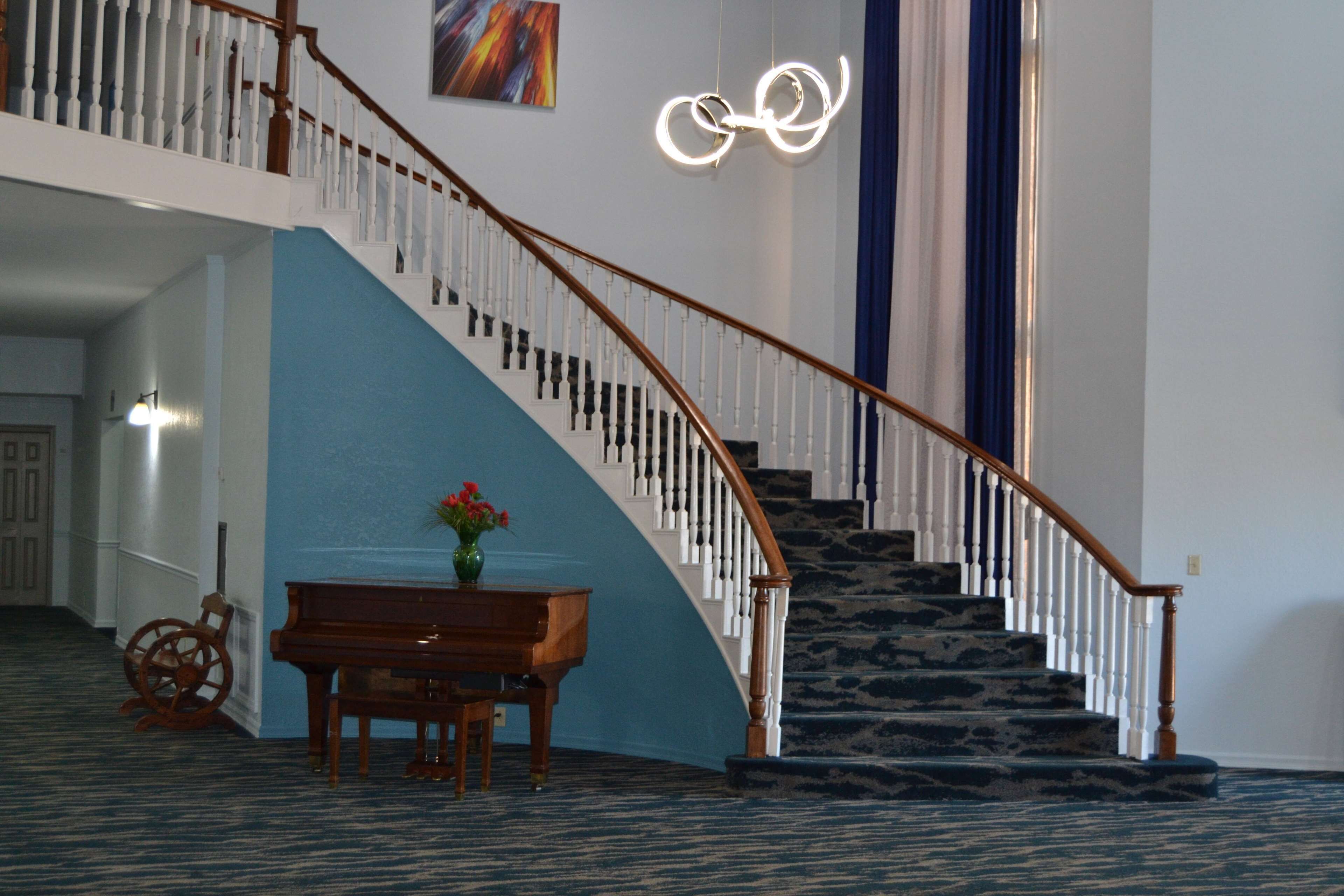 A grand staircase with a wooden handrail and white balusters, leading to an upper floor. A piano and a decorative vase with flowers are placed on the landing.