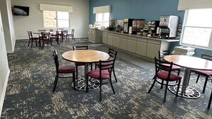 Une pièce spacieuse comprenant une grande table à manger et des chaises, un coin cuisine et un téléviseur fixé au mur.