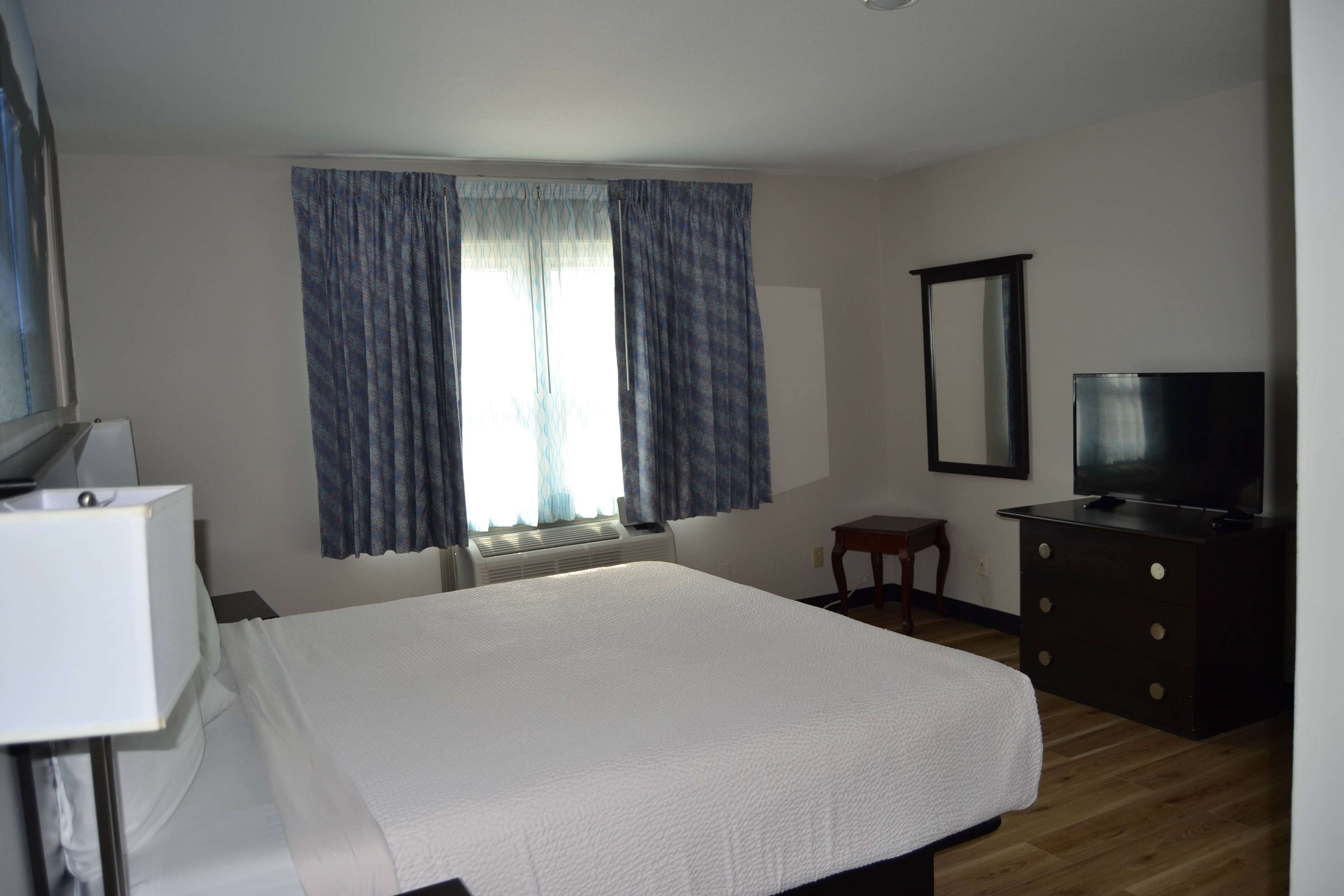 A hotel room with a bed, a TV, a small table, and a window with curtains.