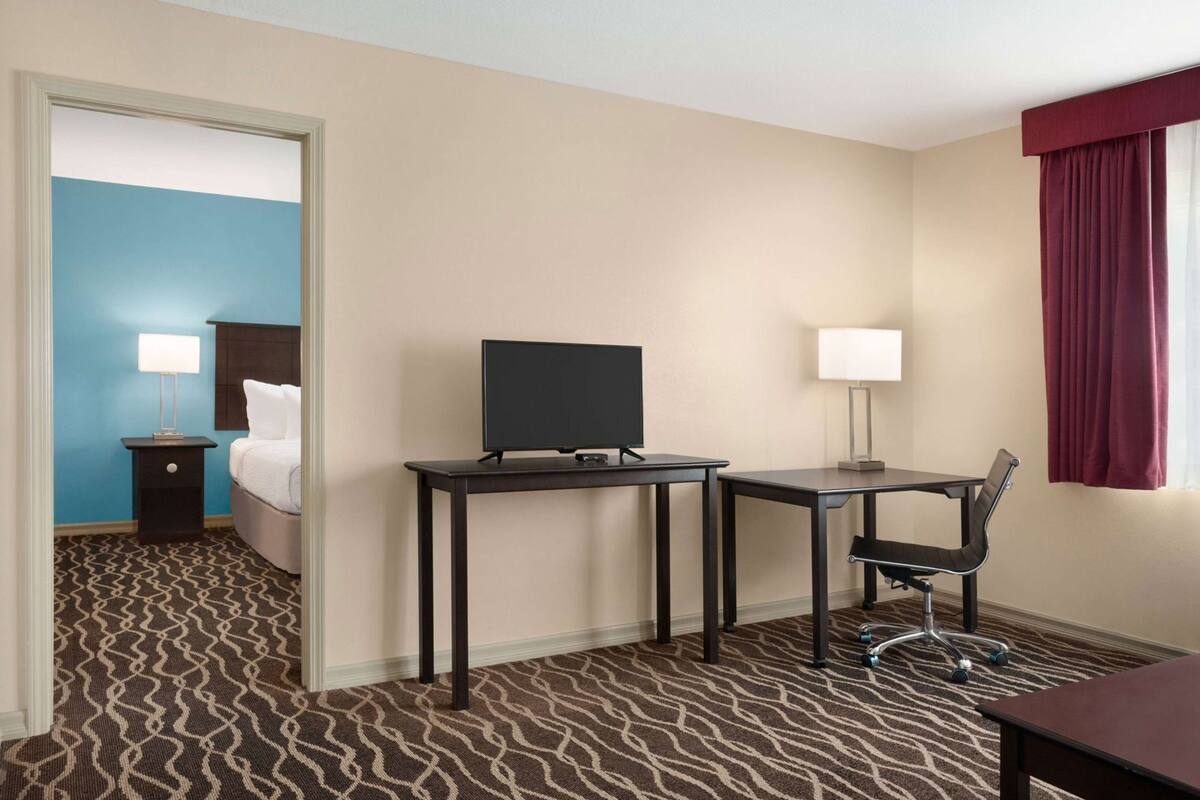 Una habitación de hotel con cama, escritorio con silla, televisor y ventana con cortinas.