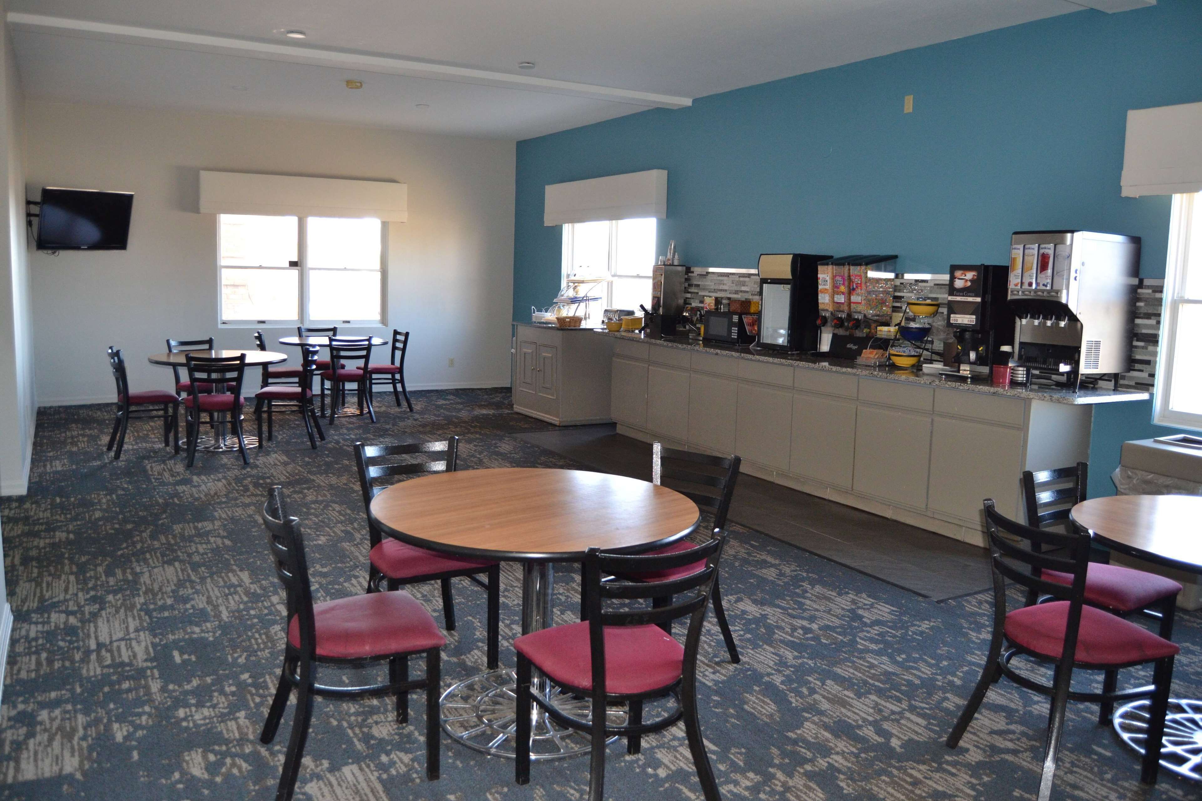 A room with a kitchen area, a TV mounted on the wall, and several tables and chairs.
