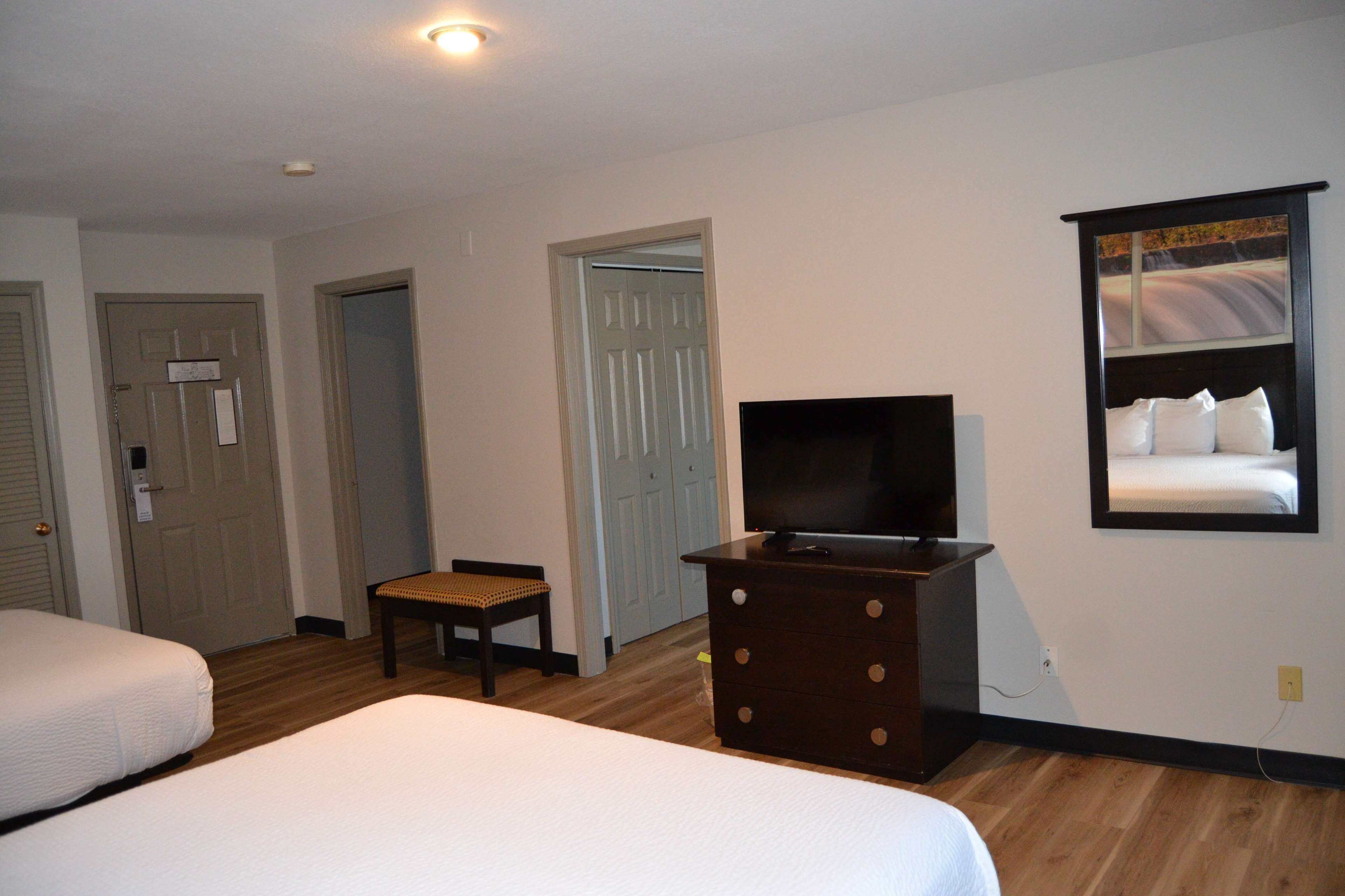Una habitación de hotel con dos camas, un televisor sobre un tocador y una puerta que da a otra habitación.