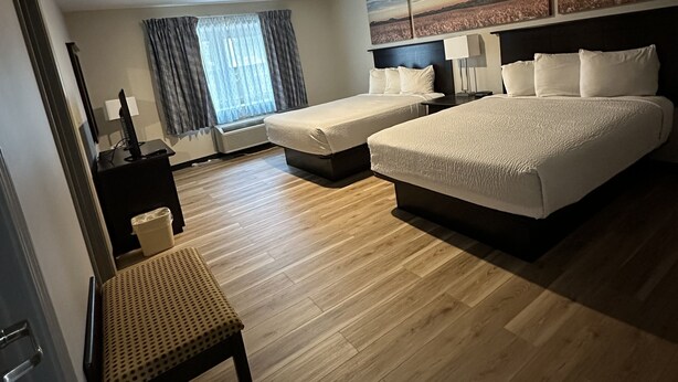 Une chambre d’hôtel moderne avec un grand lit, un plus petit lit, un bureau et une chaise. Il y a une fenêtre avec des rideaux et un tableau au mur.