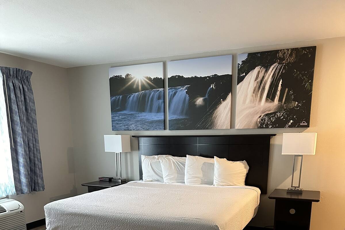 Habitación de hotel con una cama grande, una mesita de noche, una lámpara y un televisor montado en la pared.