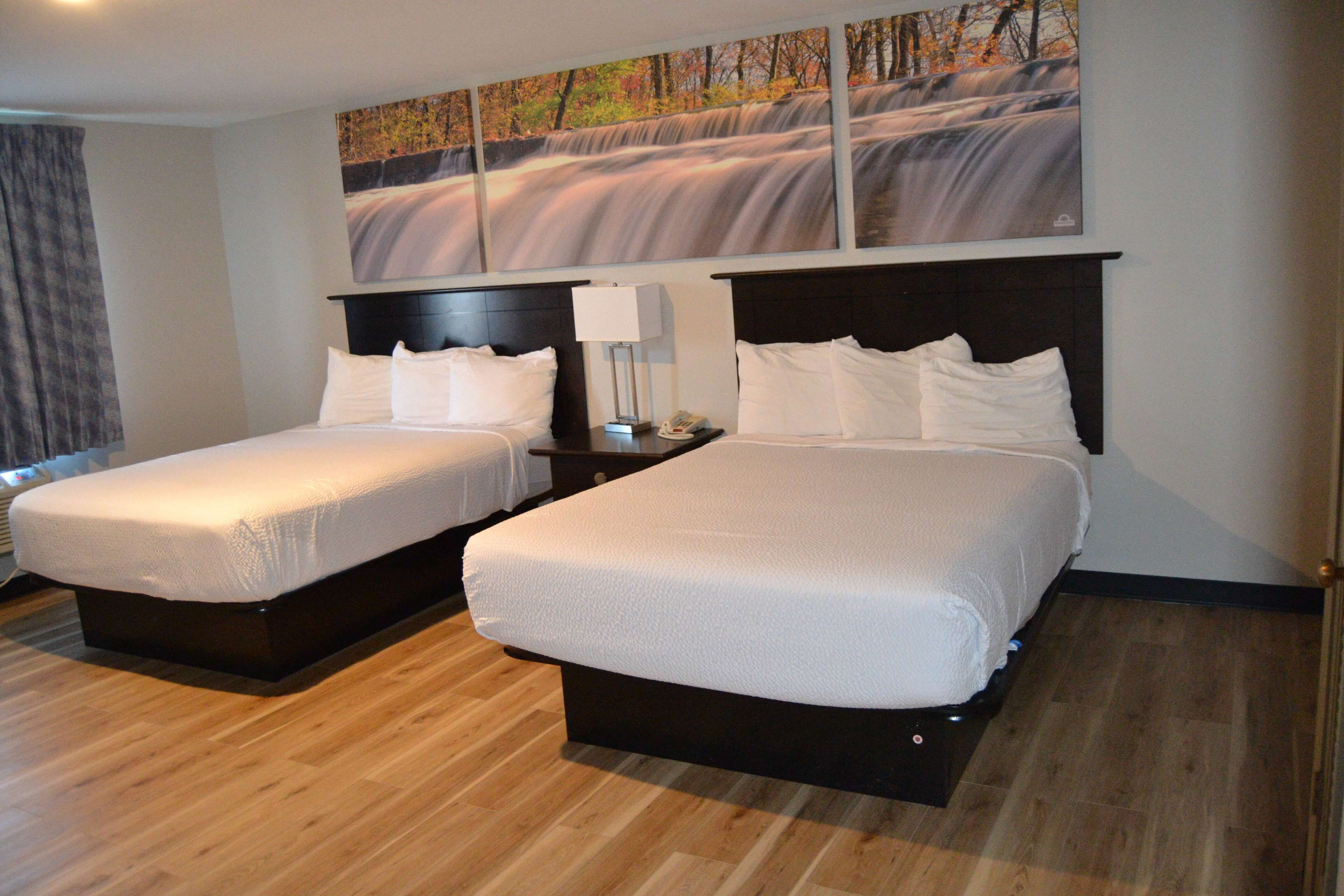 A hotel room with two beds, a painting of a waterfall on the wall, and a wooden floor.