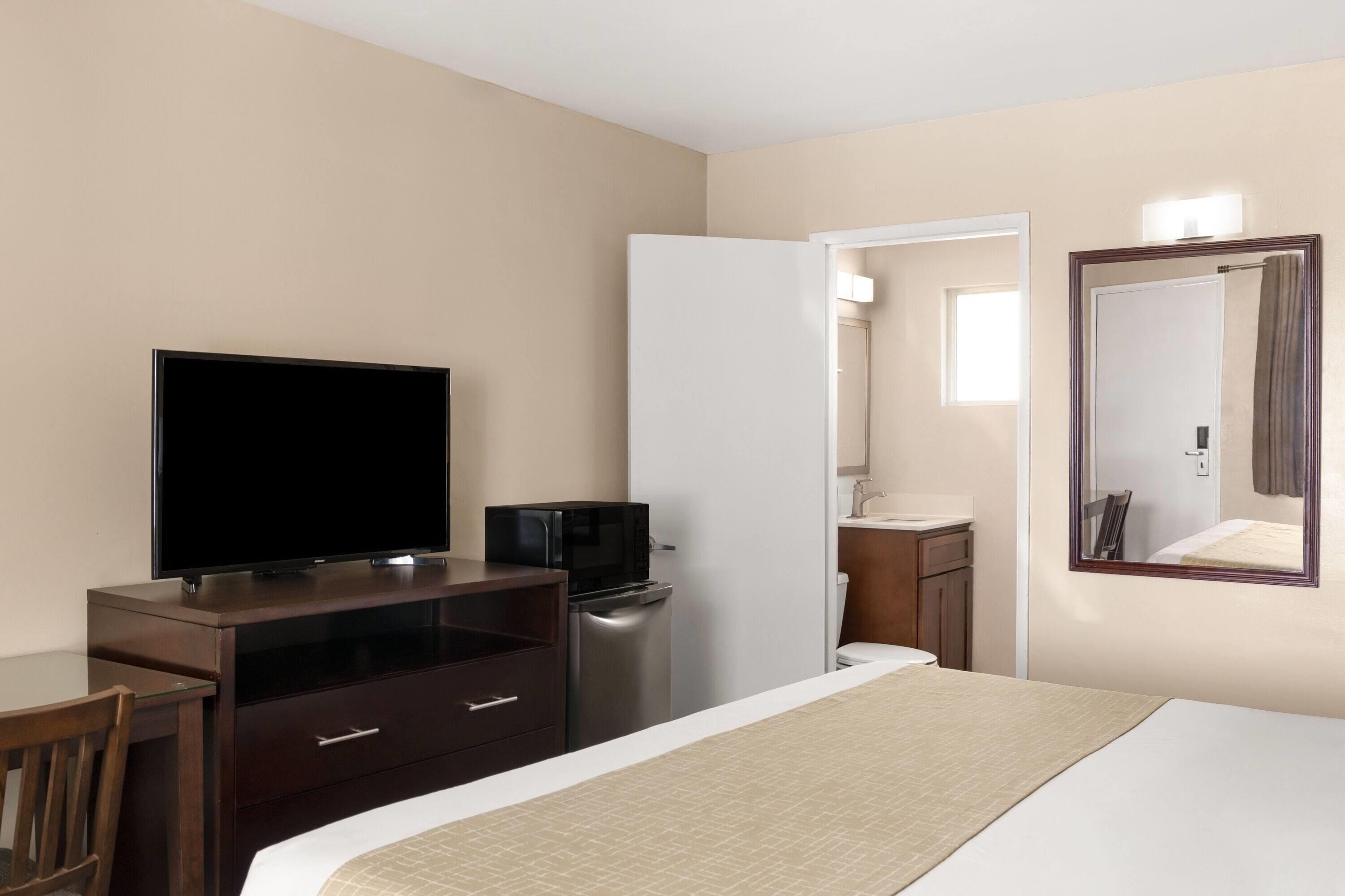 A hotel room with a bed, a TV, a microwave, a refrigerator, a desk, and a mirror.