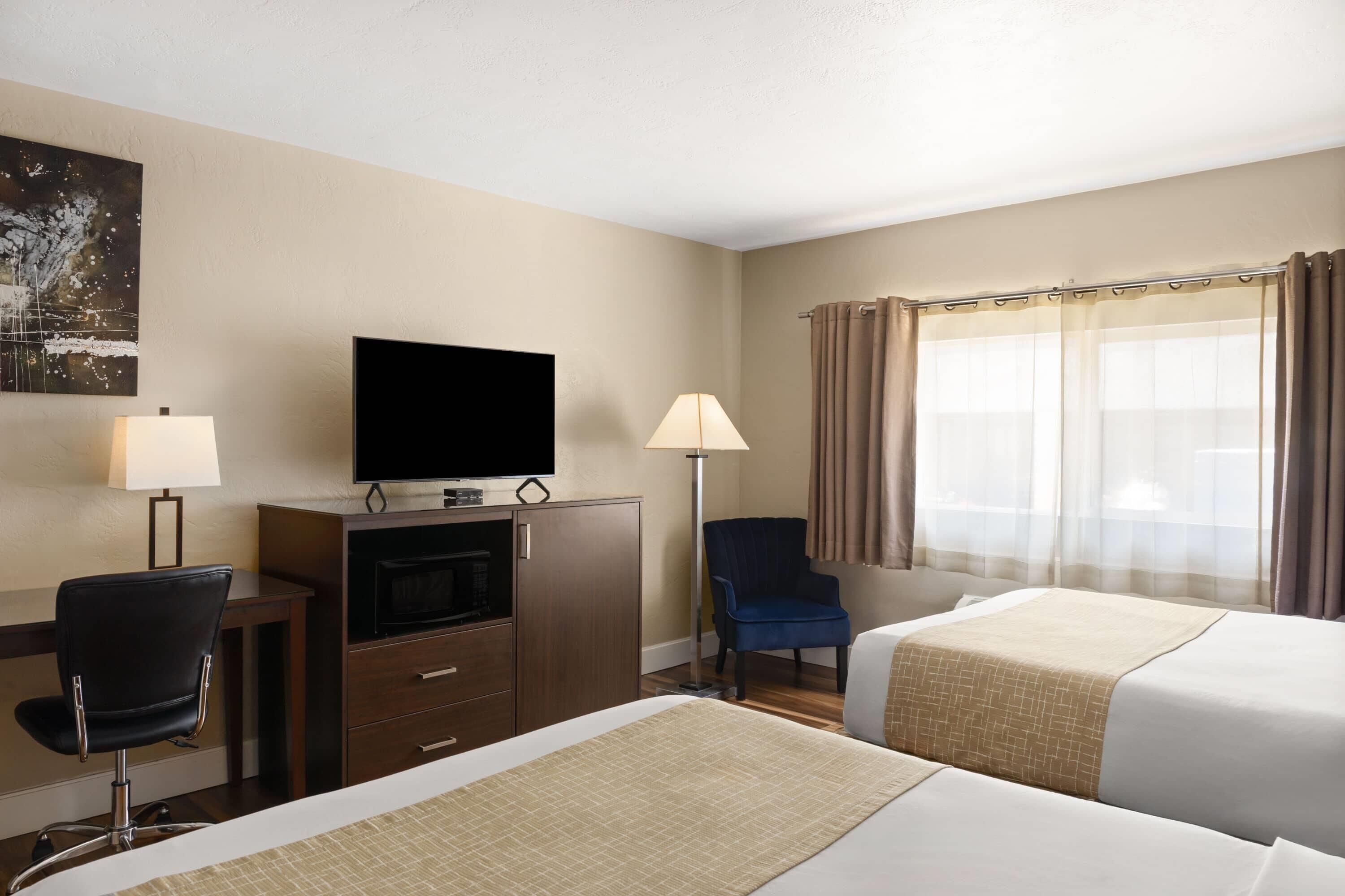 A hotel room with two beds, a desk with a TV, a chair, and a window with curtains.