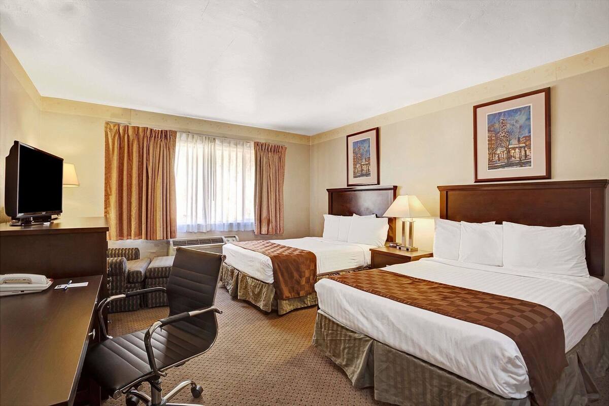 Una habitación de hotel con dos camas, un escritorio con televisor, una silla, una lámpara de escritorio y dos cuadros en la pared.