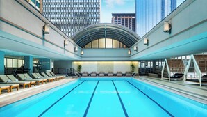 A large indoor swimming pool with multiple lanes, lounge chairs, and a modern architectural design with a glass ceiling.