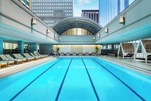 Una amplia piscina interior con varias pistas de natación, sillas de descanso y un diseño arquitectónico moderno con techo de vidrio.