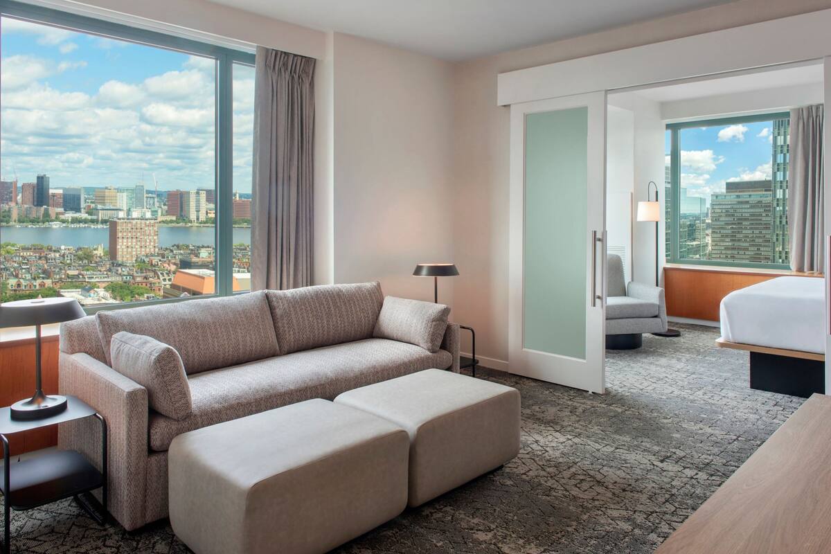 Camera d'albergo con una grande finestra vista sulla città, un divano, un letto e una poltrona.