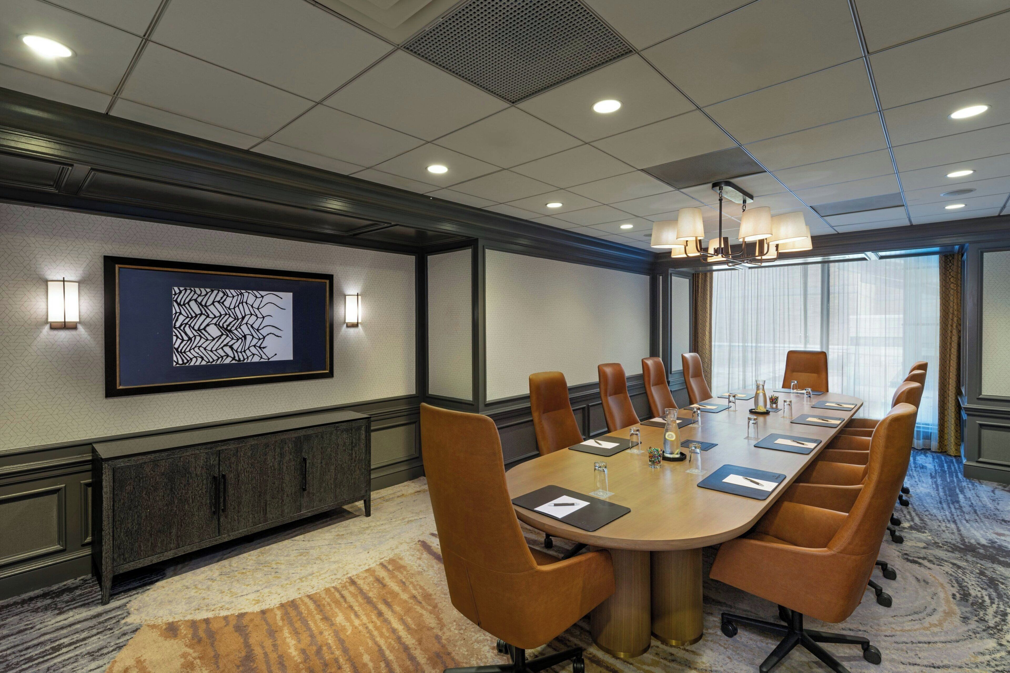 A conference room with a long table, multiple chairs, a cabinet, and a framed artwork on the wall.