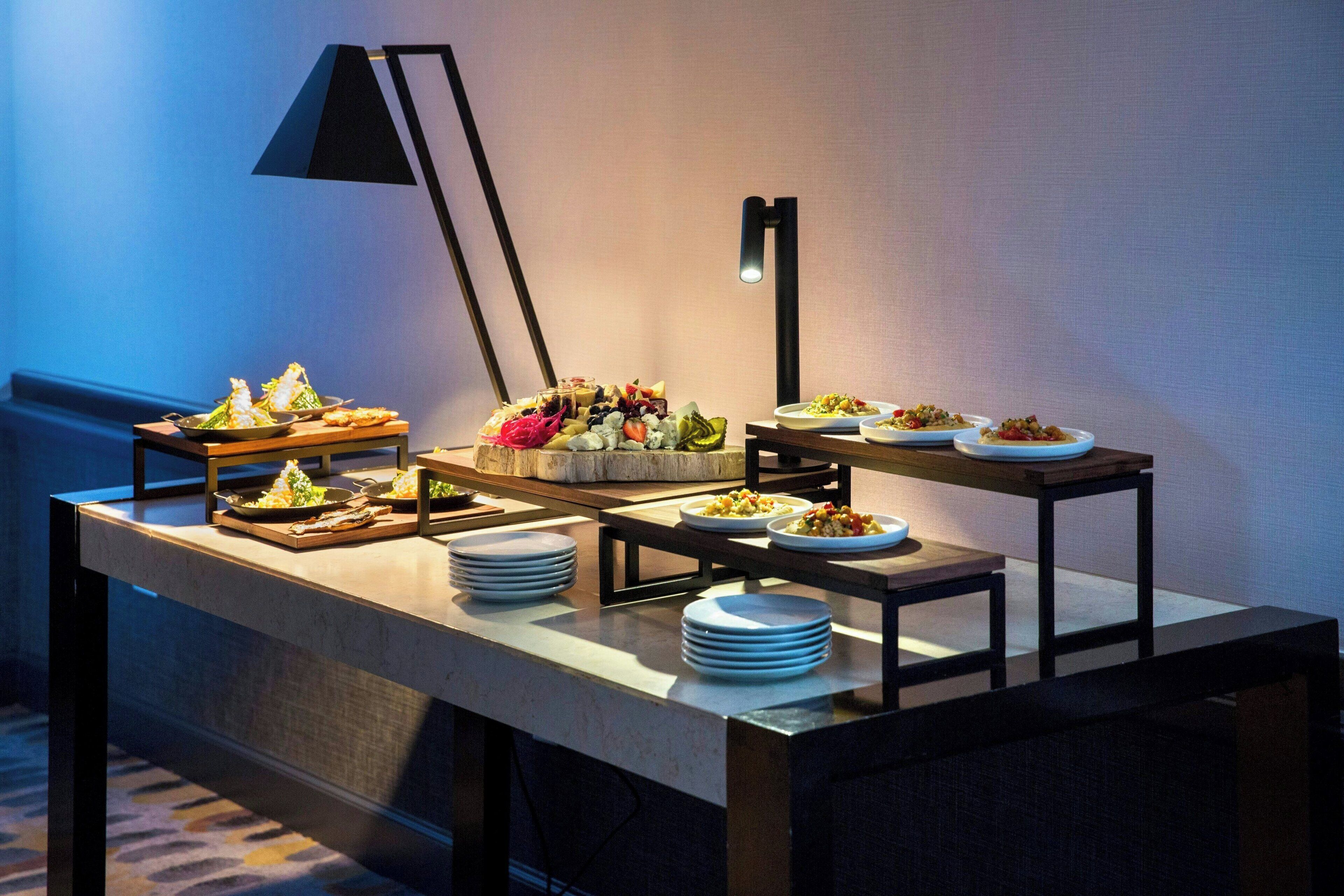 A buffet setup with various dishes and plates, a lamp, and a wall-mounted light fixture.