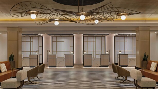 A lobby with a geometric patterned floor, modern furniture, and a unique ceiling design with hanging lights.