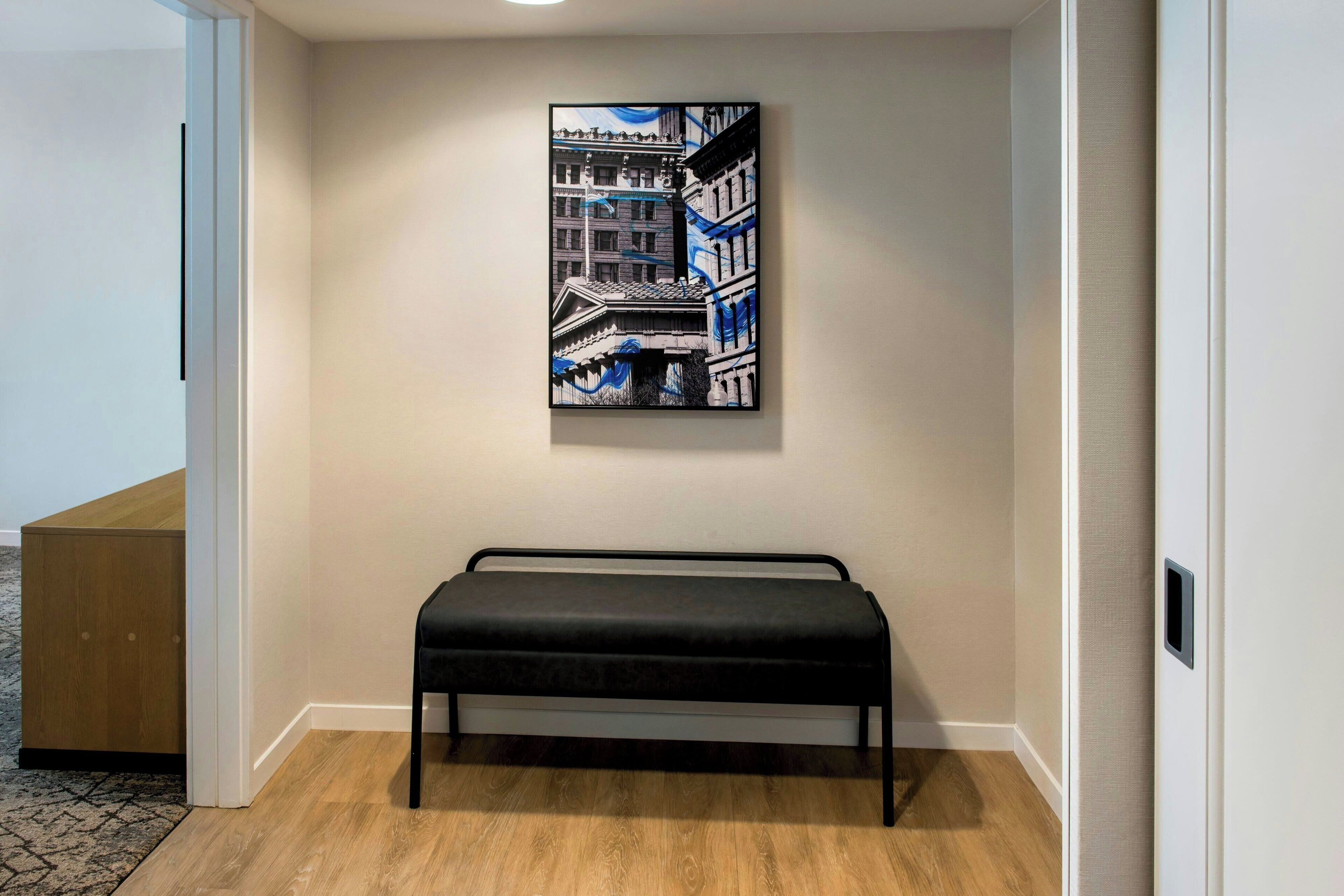 A hallway with a bench, a painting on the wall, and a wooden cabinet.