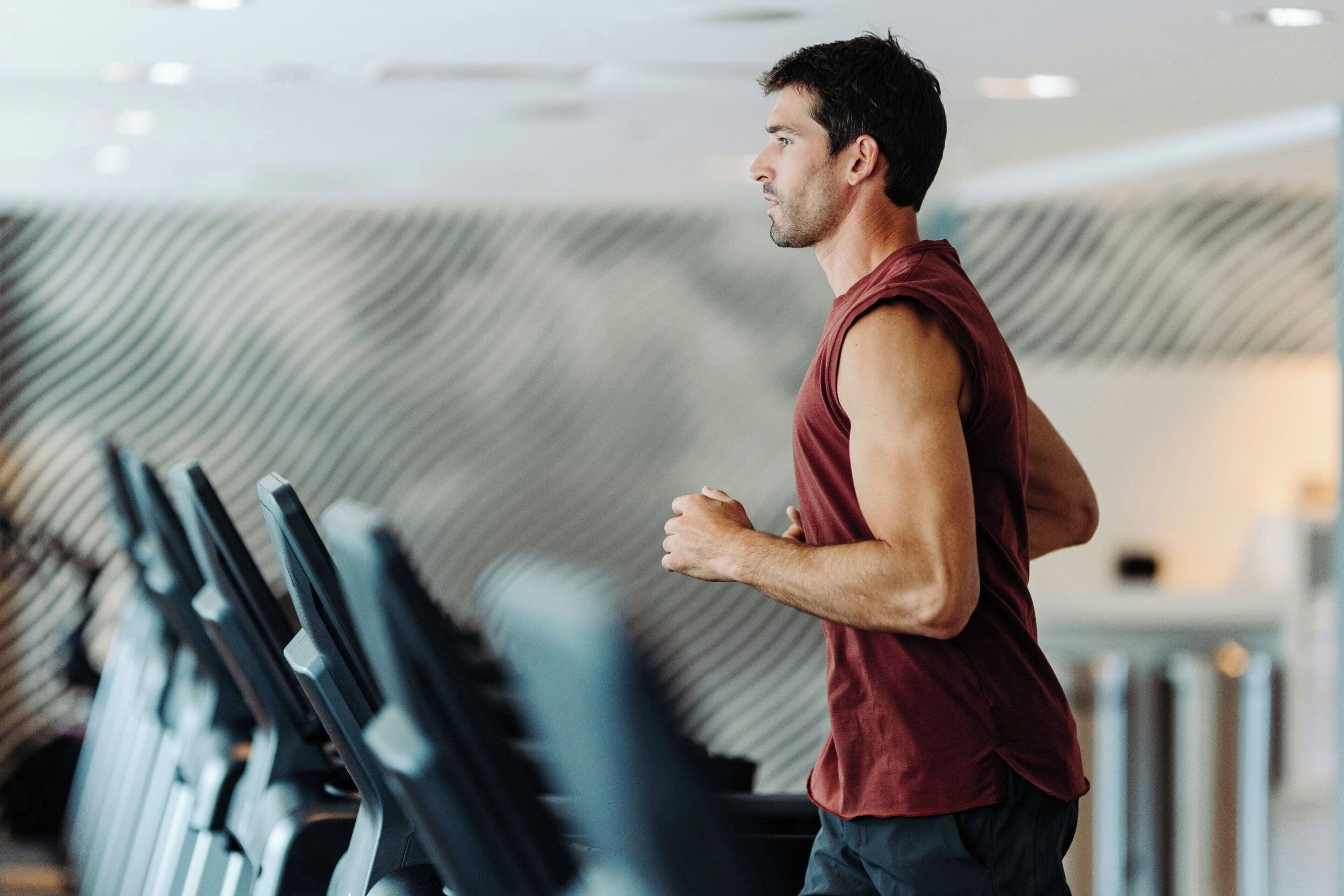 Een man rent op een loopband in een fitnessruimte met een modern design en een behanget achtergrond.