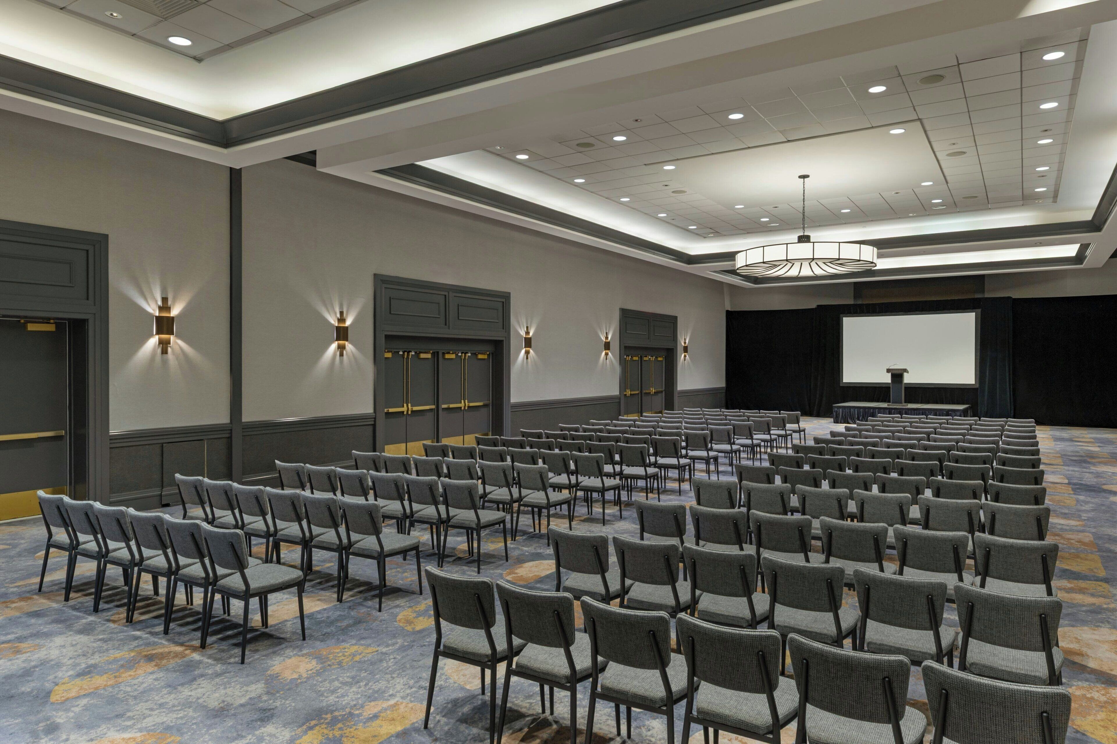 A conference room with rows of chairs, a projector screen, and a stage.