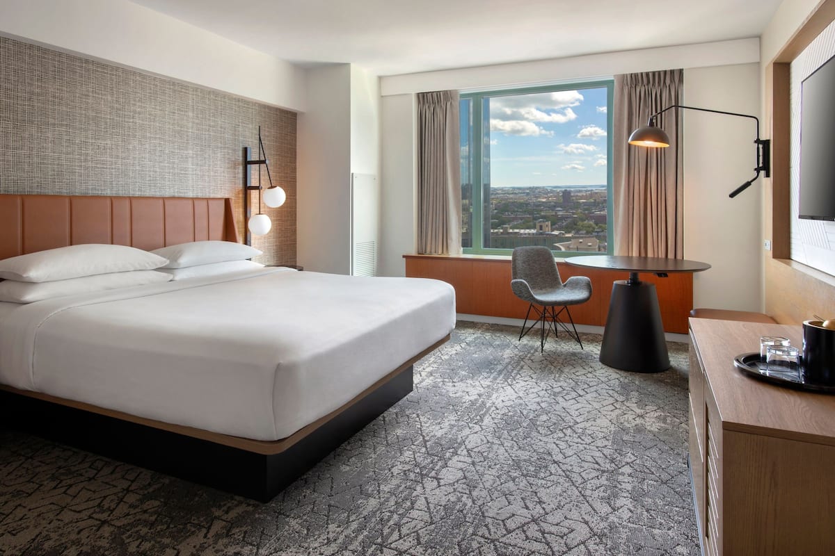 Camera d'albergo con un letto grande, una scrivania con una sedia, una televisione e una finestra con vista sulla città.