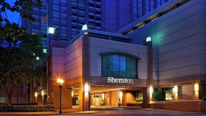 A Sheraton hotel entrance with a large arched doorway, a prominent sign, and a well-lit facade.