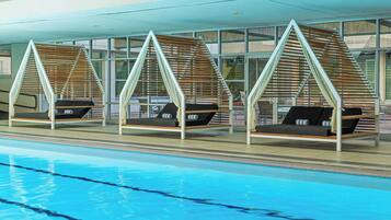 Un espace aménagé au bord de la piscine, avec trois chaises longues disposées sous une pergola en bois, une piscine à l’eau d’un bleu limpide et la façade d’un bâtiment moderne dotée de grandes fenêtres.