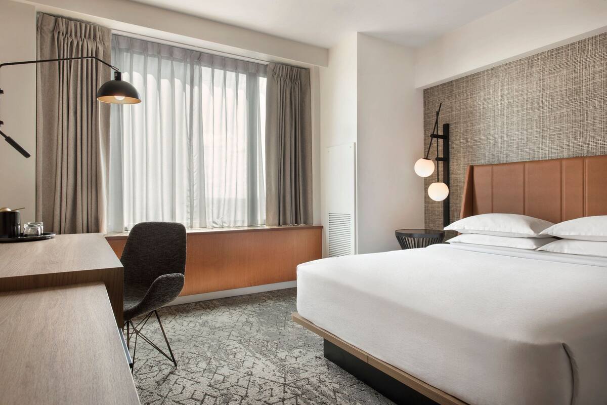 Una camera d'albergo con un letto grande, una scrivania, una sedia e una finestra con tende.