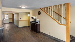 A spacious hallway with wooden flooring, a kitchen area with dark cabinets, and a wooden staircase. - Red Roof Inn Des Moines (Des Moines)