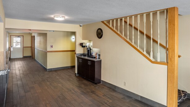 A spacious hallway with wooden flooring, a kitchen area with dark cabinets, and a wooden staircase. - Red Roof Inn Des Moines (Des Moines)