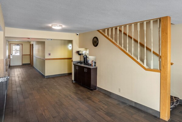 Un hall d’entrée spacieux avec un plancher en bois, un coin cuisine doté de meubles sombres et un escalier en bois.