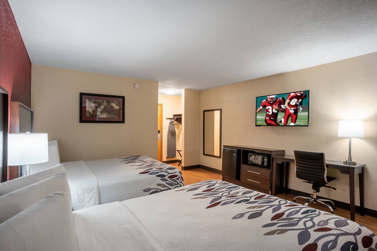 A hotel room with two beds, a desk, a chair, a TV, and a mirror.