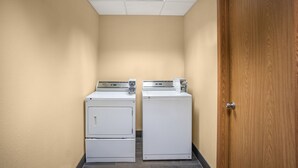 A laundry room with two stacked washers and dryers, a wooden door, and a tiled floor. - Red Roof Inn Des Moines (Des Moines)