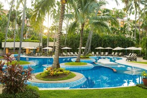 Un área de piscina con varias secciones circulares, palmeras y sillones de descanso.