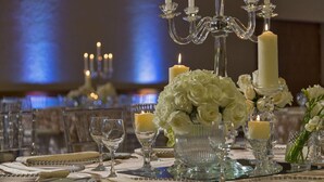 Una mesa de comedor formal adornada con cristalería, velas y flores blancas.