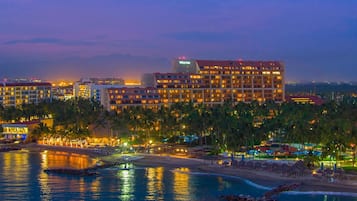 Un hotel de varios pisos, una playa en primer plano y palmeras.
