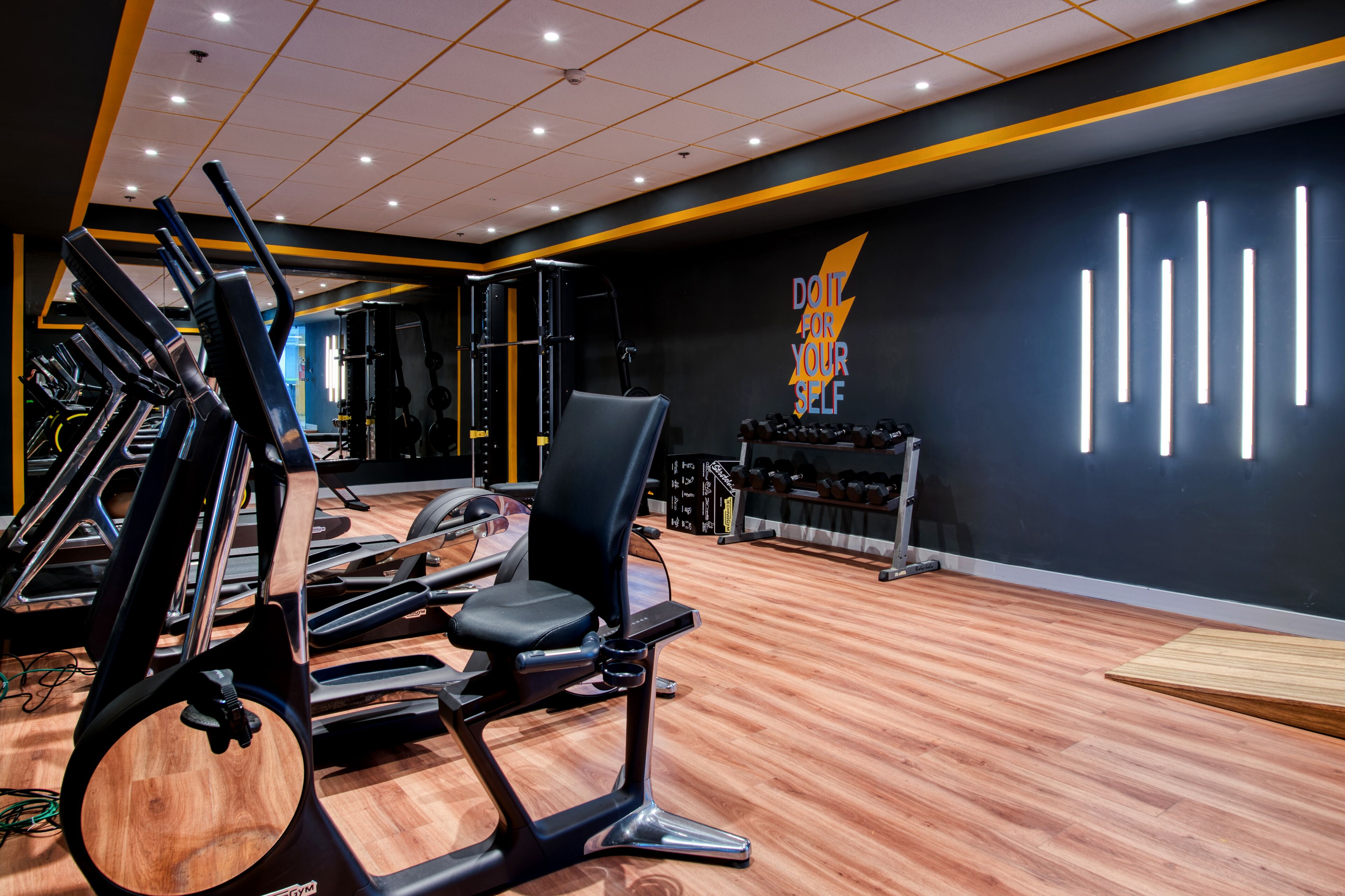 A gym with exercise equipment, a wall with motivational text, and a wooden floor.