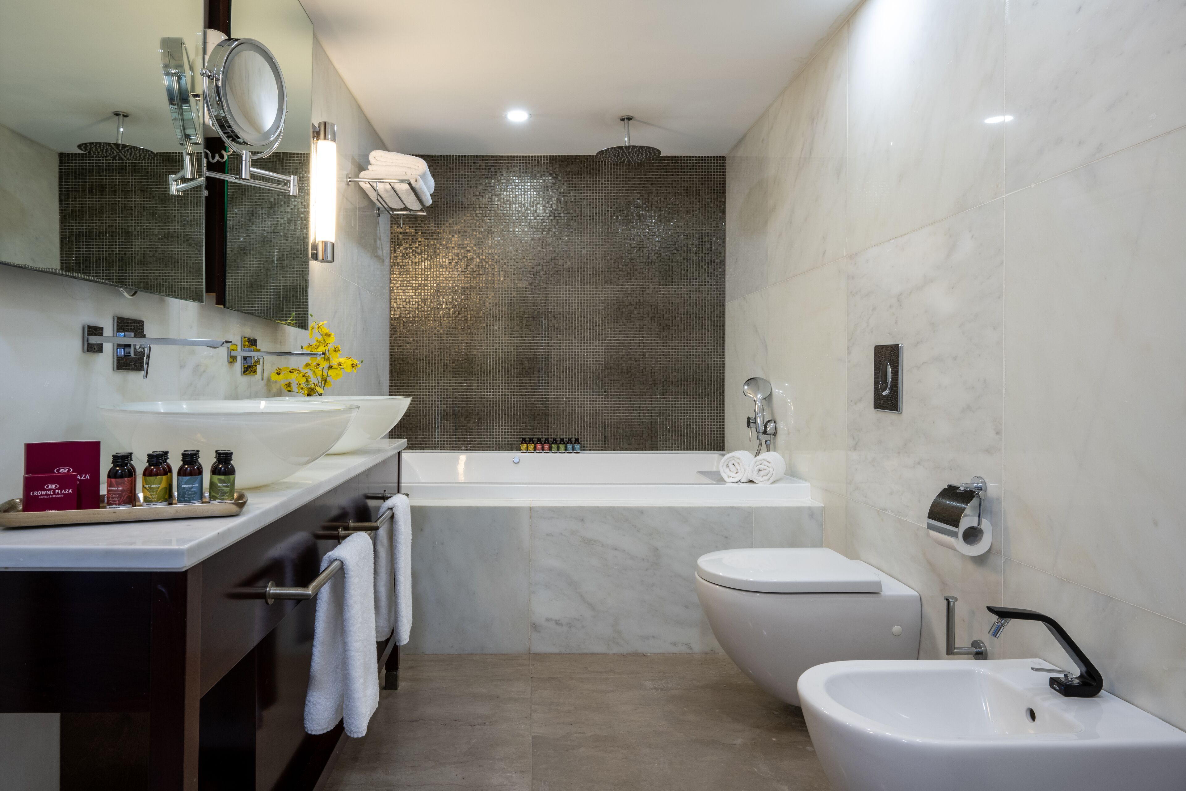 A modern bathroom with a large bathtub, a separate toilet, and a sink. There is a mirror above the sink, and a towel rack is visible.