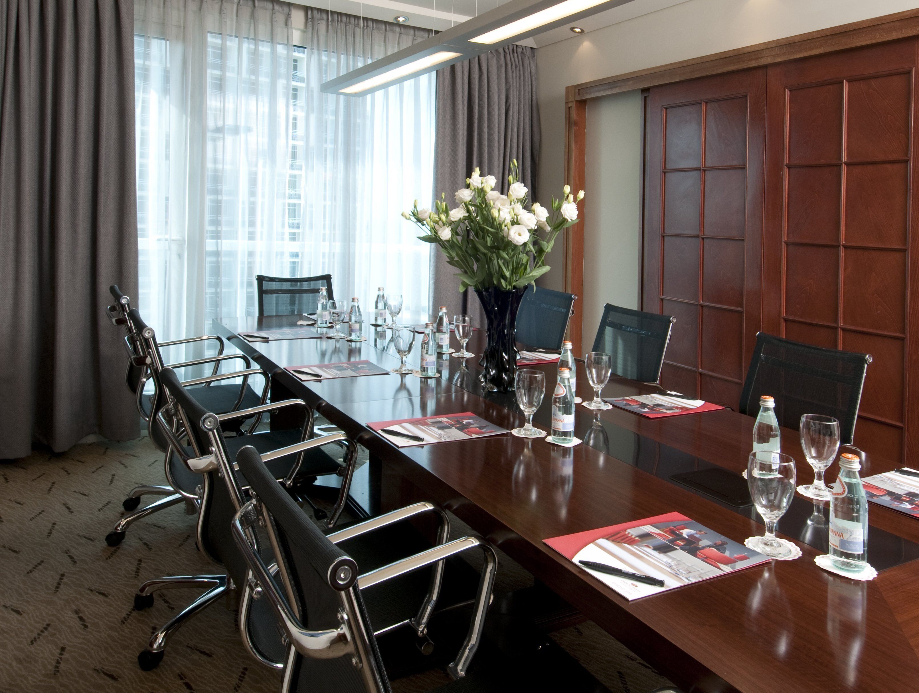 A conference room with a long table, chairs, and a vase of flowers.