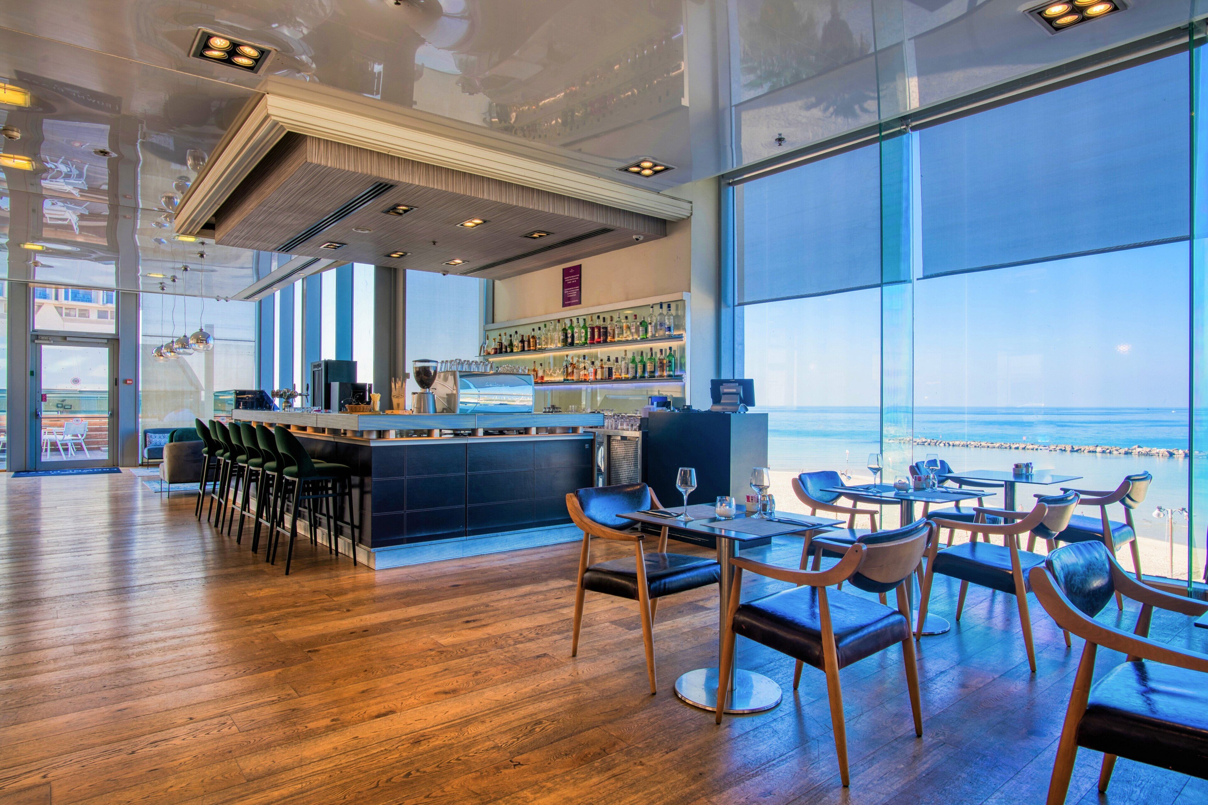 A modern bar area with a view of the ocean, wooden flooring, and bar stools.