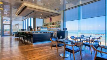 A modern bar area with a view of the ocean, wooden flooring, and bar stools.