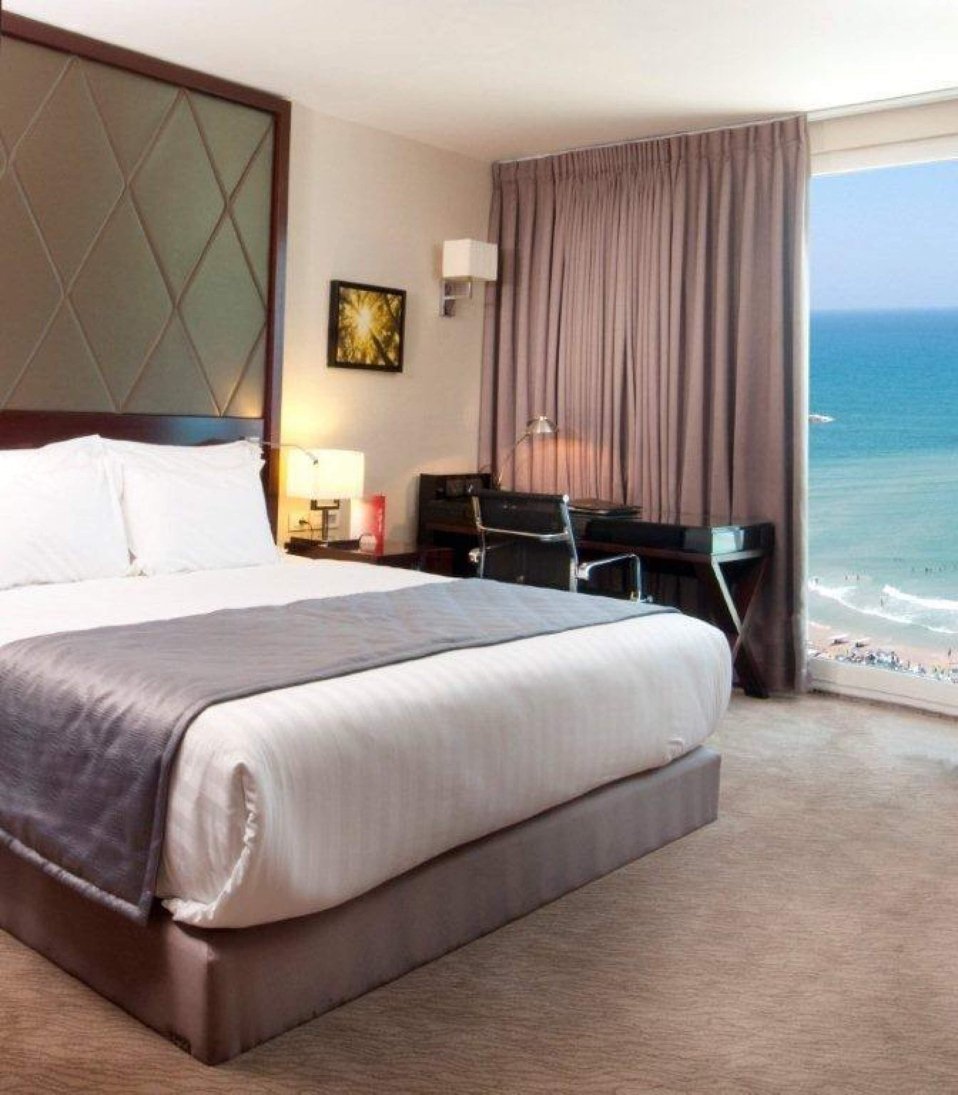 Camera d'albergo con un grande letto, una scrivania, una sedia, una lampada e vista sull'oceano.