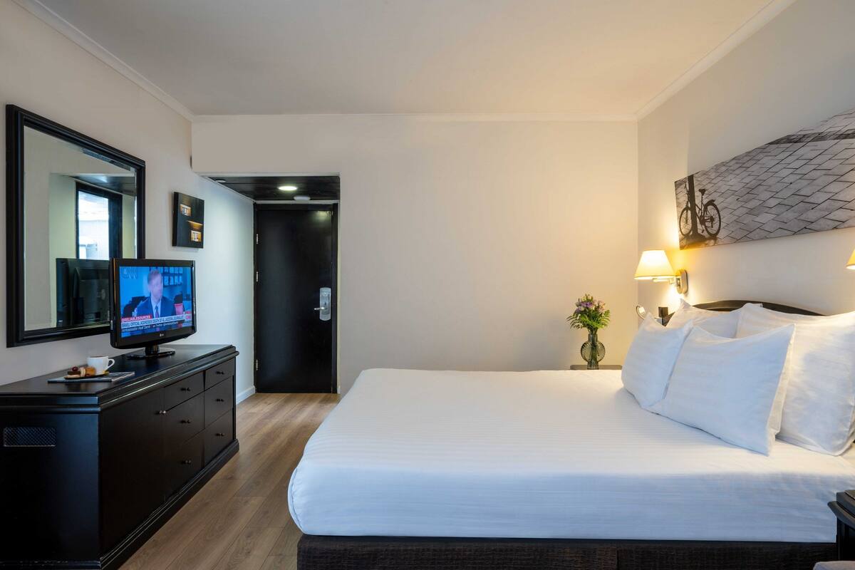 Une chambre d’hôtel avec un grand lit, un téléviseur posé sur une commode, un miroir et une lampe fixée au mur.
