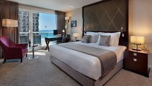 A hotel room with a large bed, a desk with a computer, a red chair, and a view of the ocean. - Crowne Plaza Tel Aviv Beach by IHG (Tel Aviv)