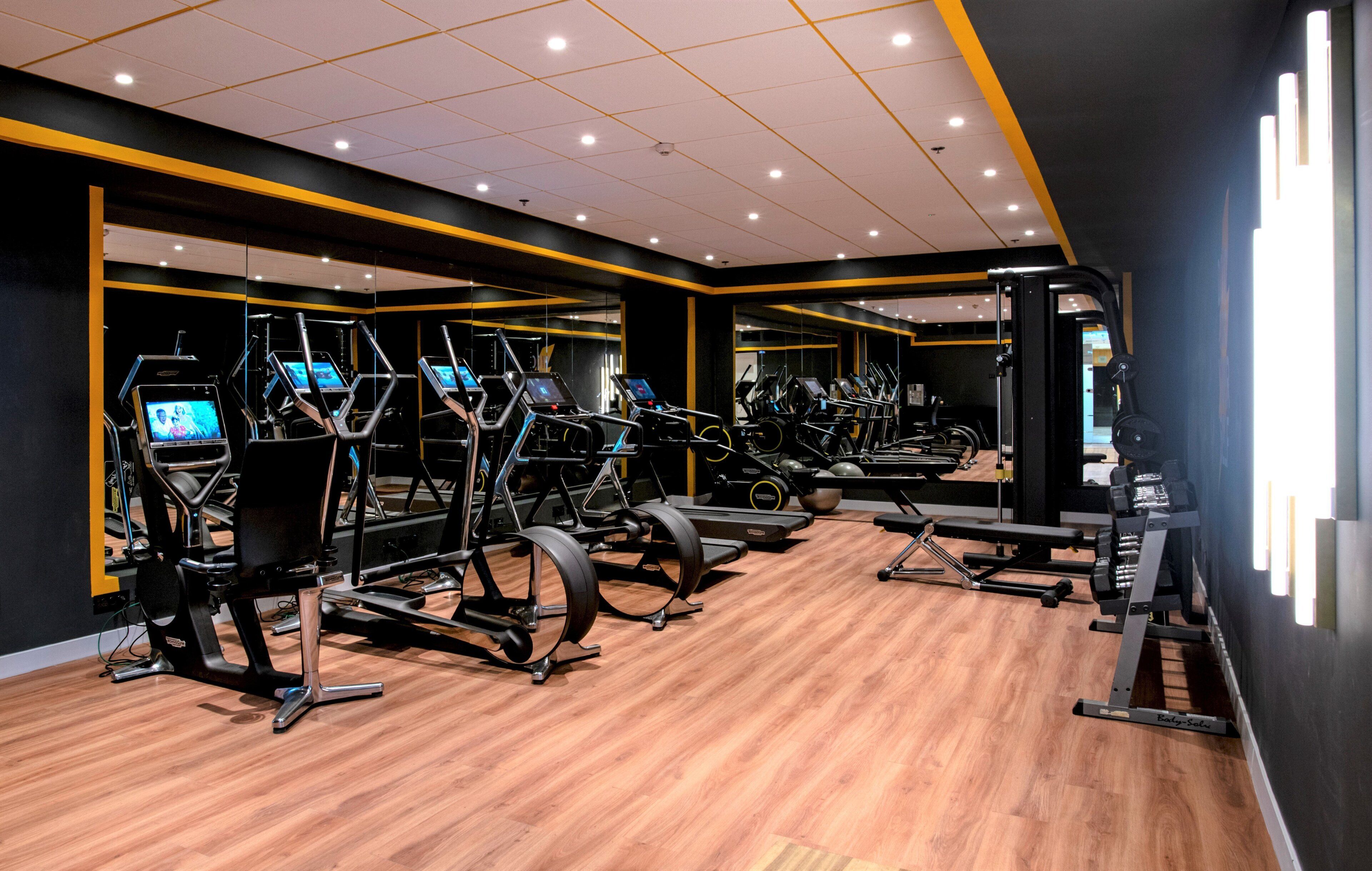 A gym with multiple exercise machines, wooden flooring, and mirrored walls.