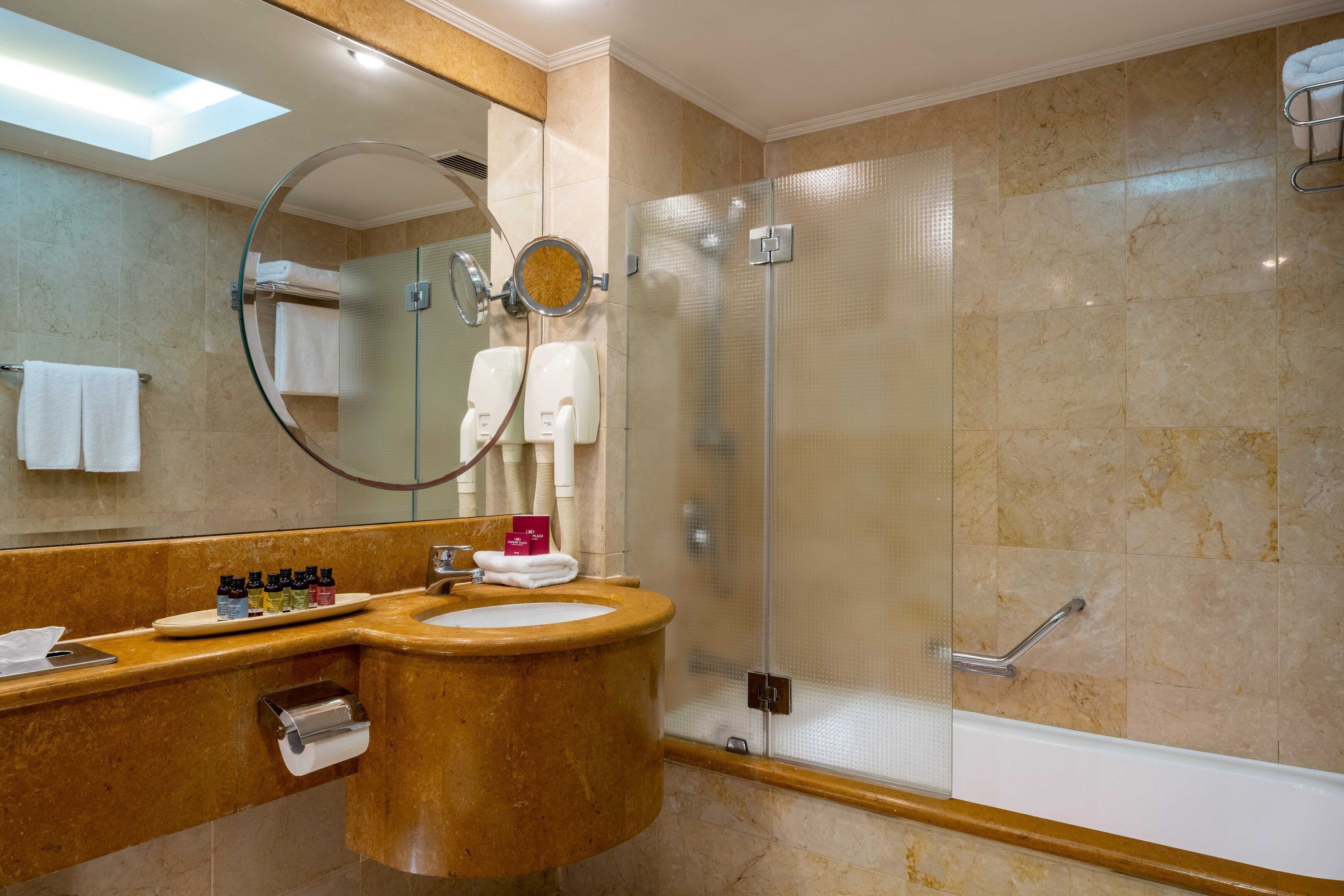 A modern bathroom with a marble sink, a large mirror, and a glass-enclosed shower.