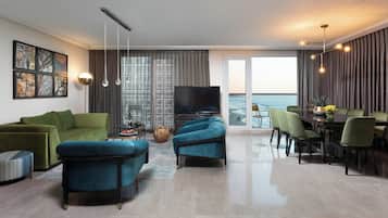 A modern living room with a sofa, chairs, a TV, and a dining area with a view of the sea.